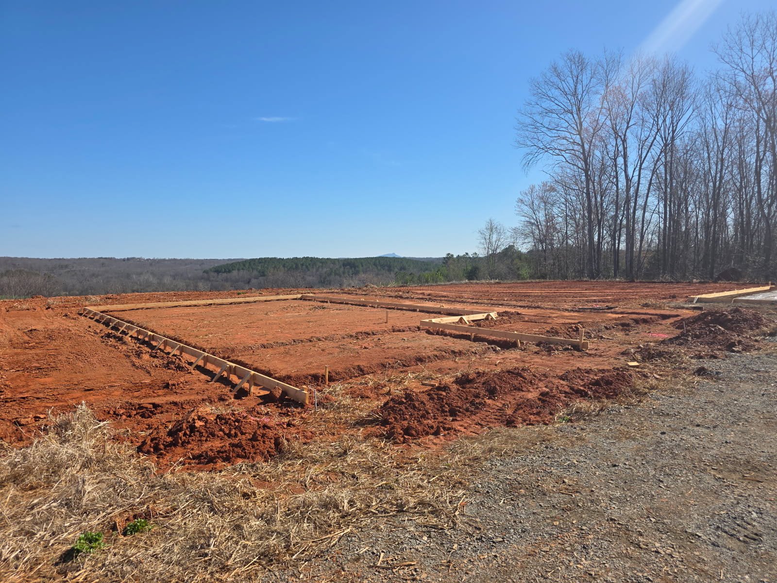Excavated trench and plumbing service area at a new residential build in Yadkinville, NC, showing underground rough-in work for water and drain lines by Burcham's Plumbing.
