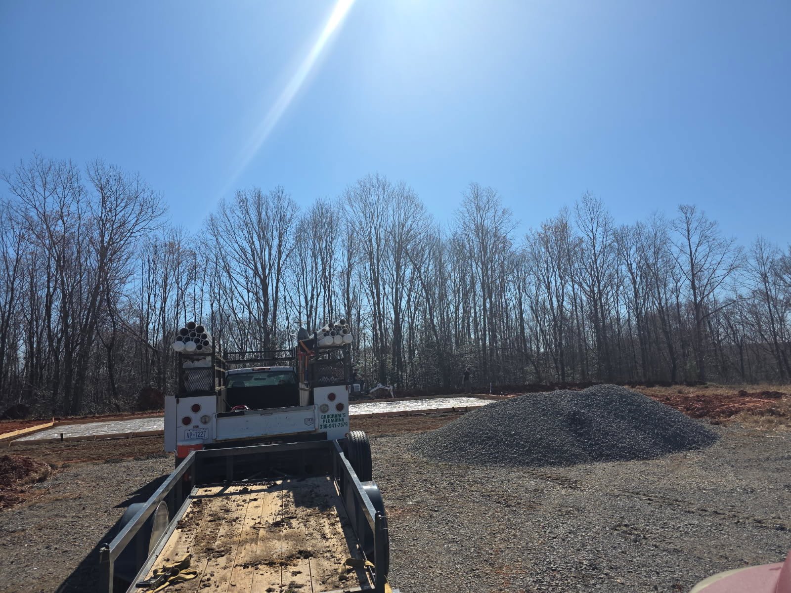 Job site overview of new construction plumbing with open trenching, soil staging, and supply routing for a single-family home in the Piedmont Triad.