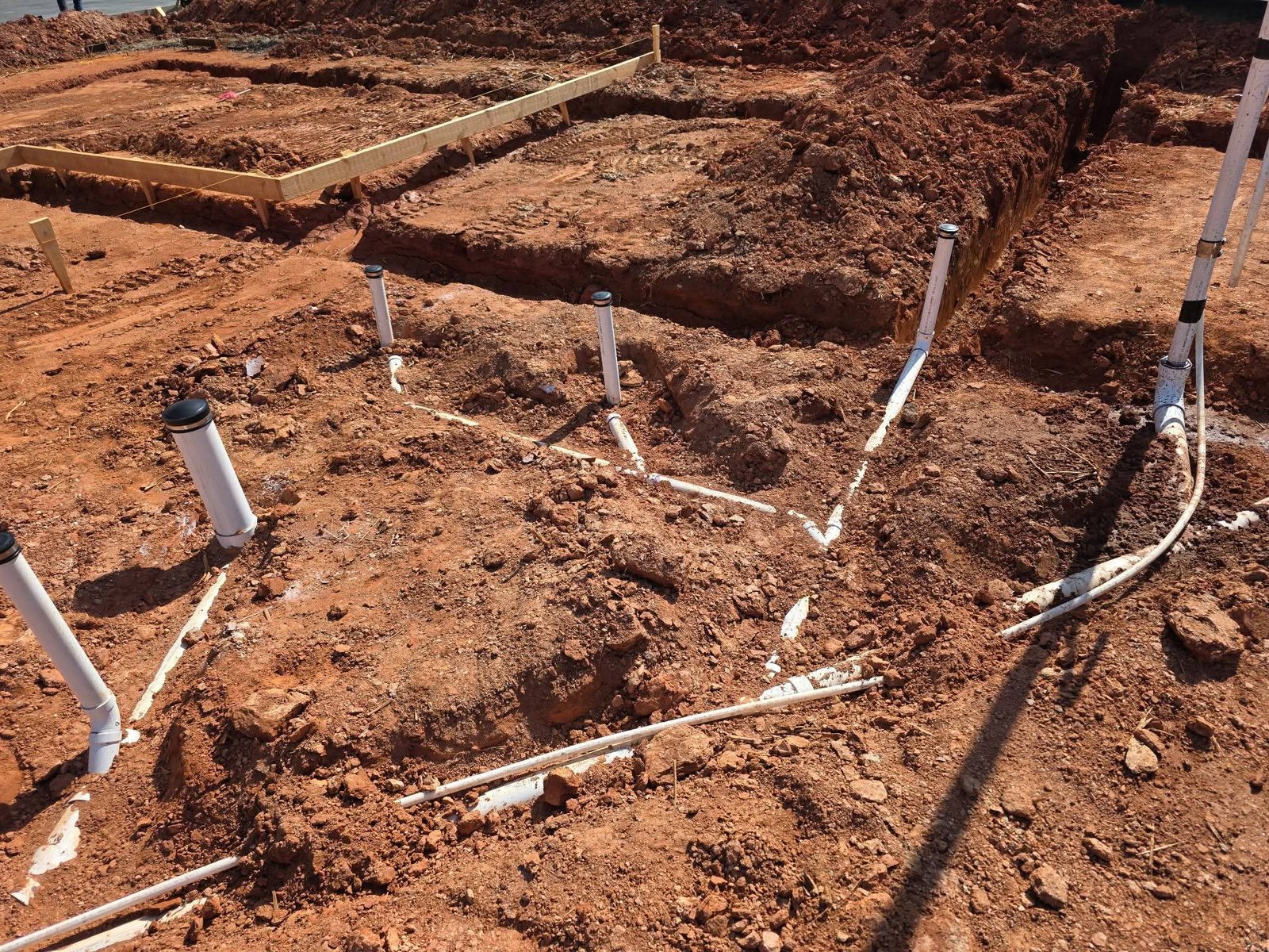 Installed underground plumbing with protected piping at a new house construction site, ready for backfill and inspection.