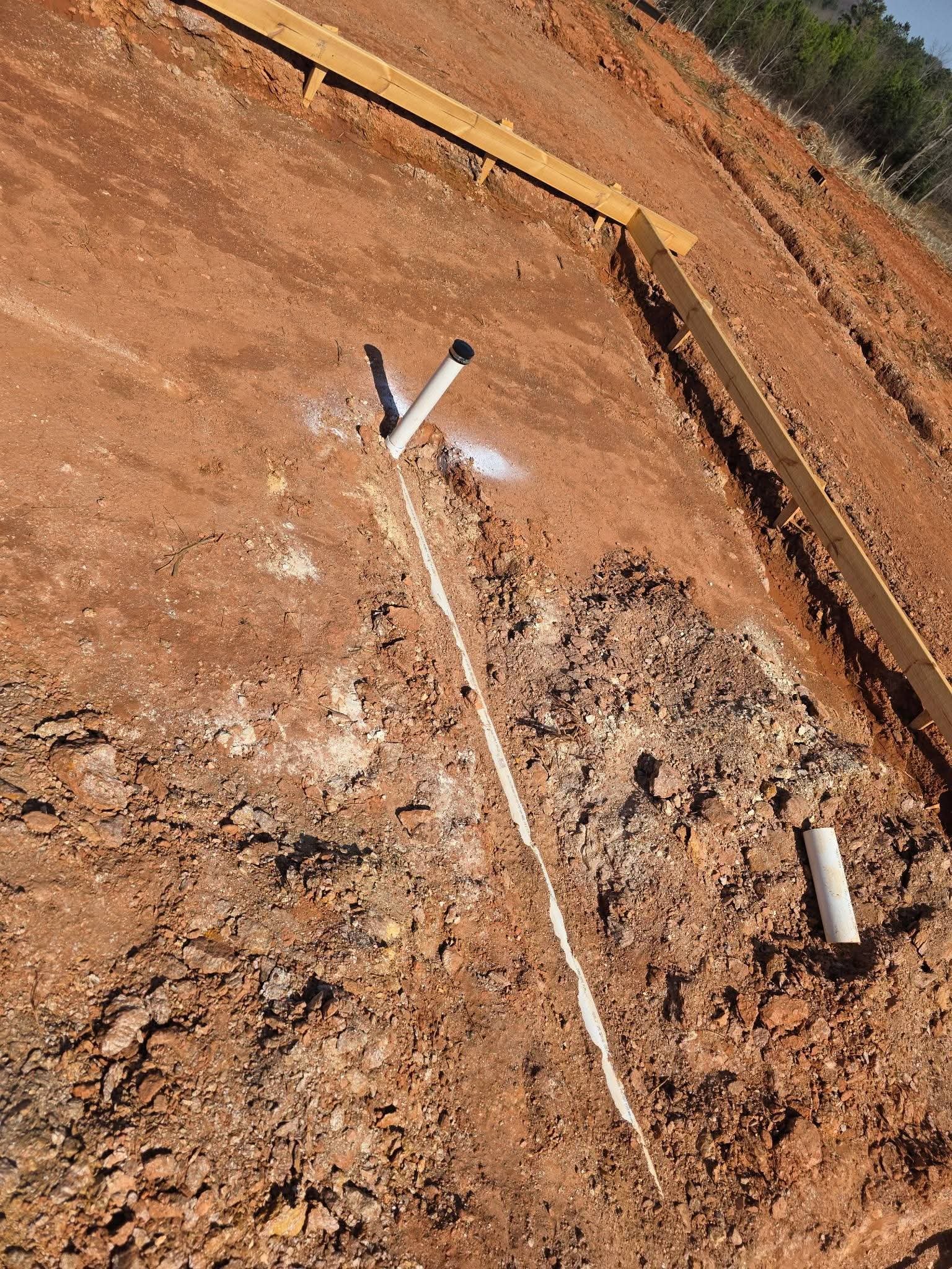 Partially backfilled underground plumbing with concealed sections and visible inspection points for new construction rough-in.