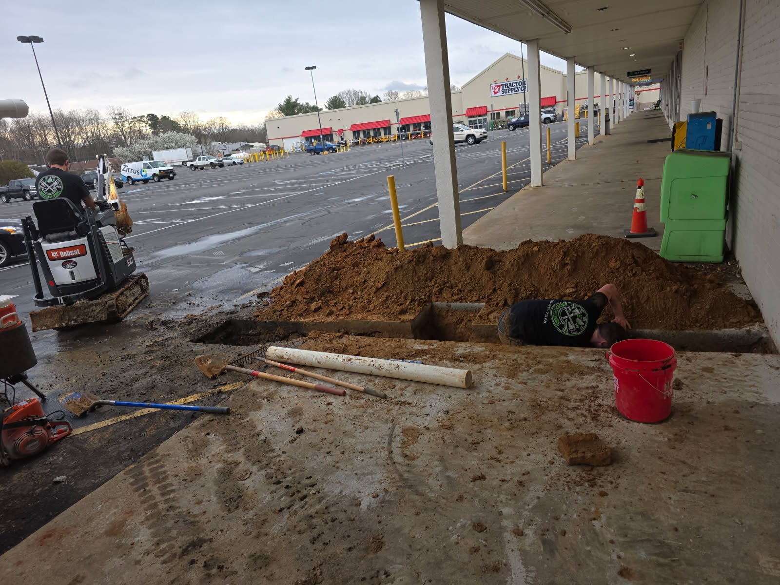 Commercial plumbing excavation at a fitness facility showing soil removal and alignment for main sewer and water routes.