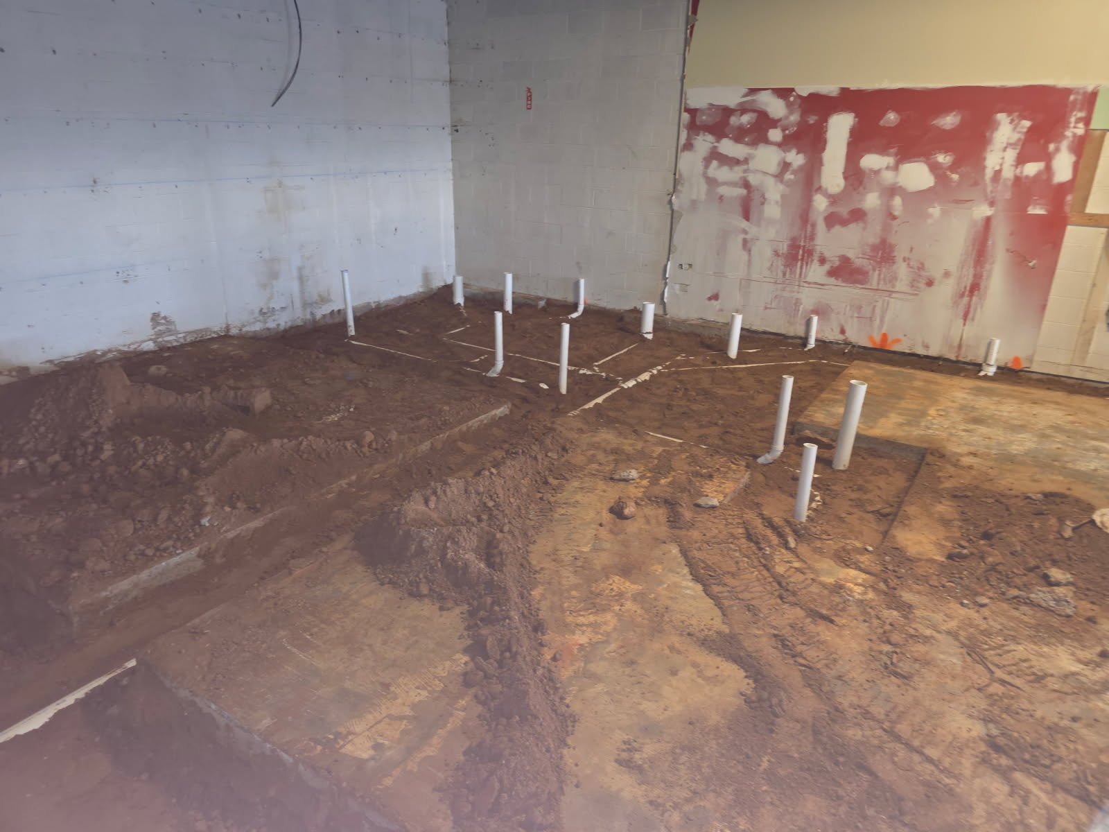 Installed underground plumbing lines inside a commercial gym shell with protected piping before finishes.