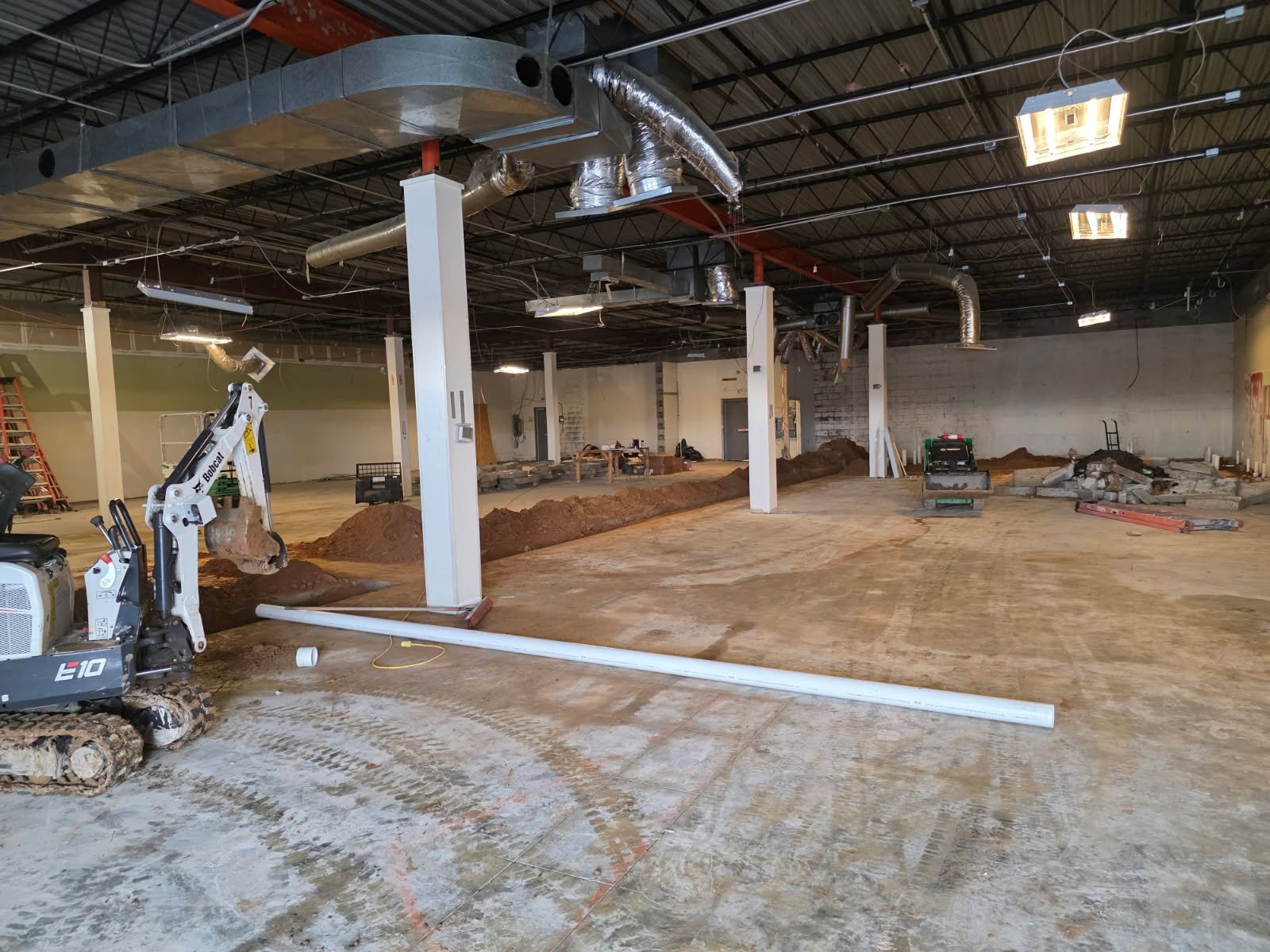 Final prep for underground plumbing install inside the gym footprint with clean trenches and staged materials.