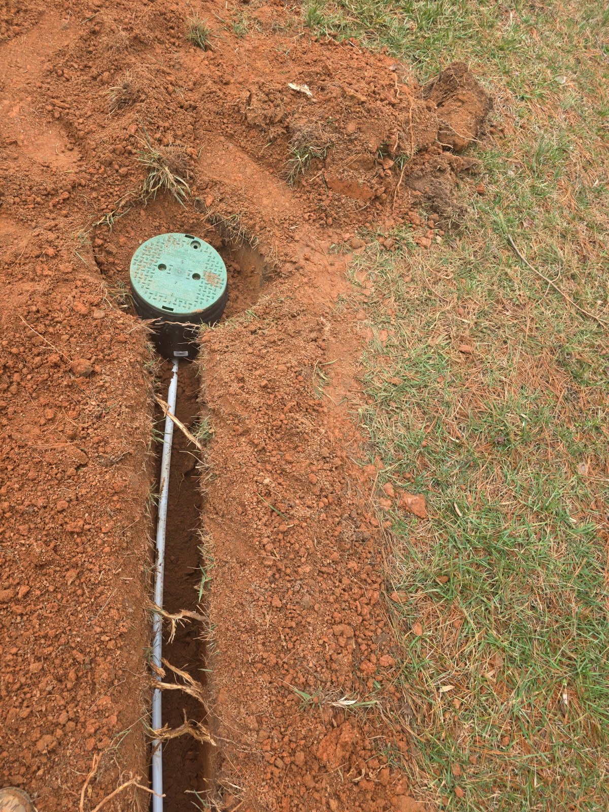 Exterior underground utility install showing septic or irrigation-related trench work adjacent to waterline routing in the Triad area.